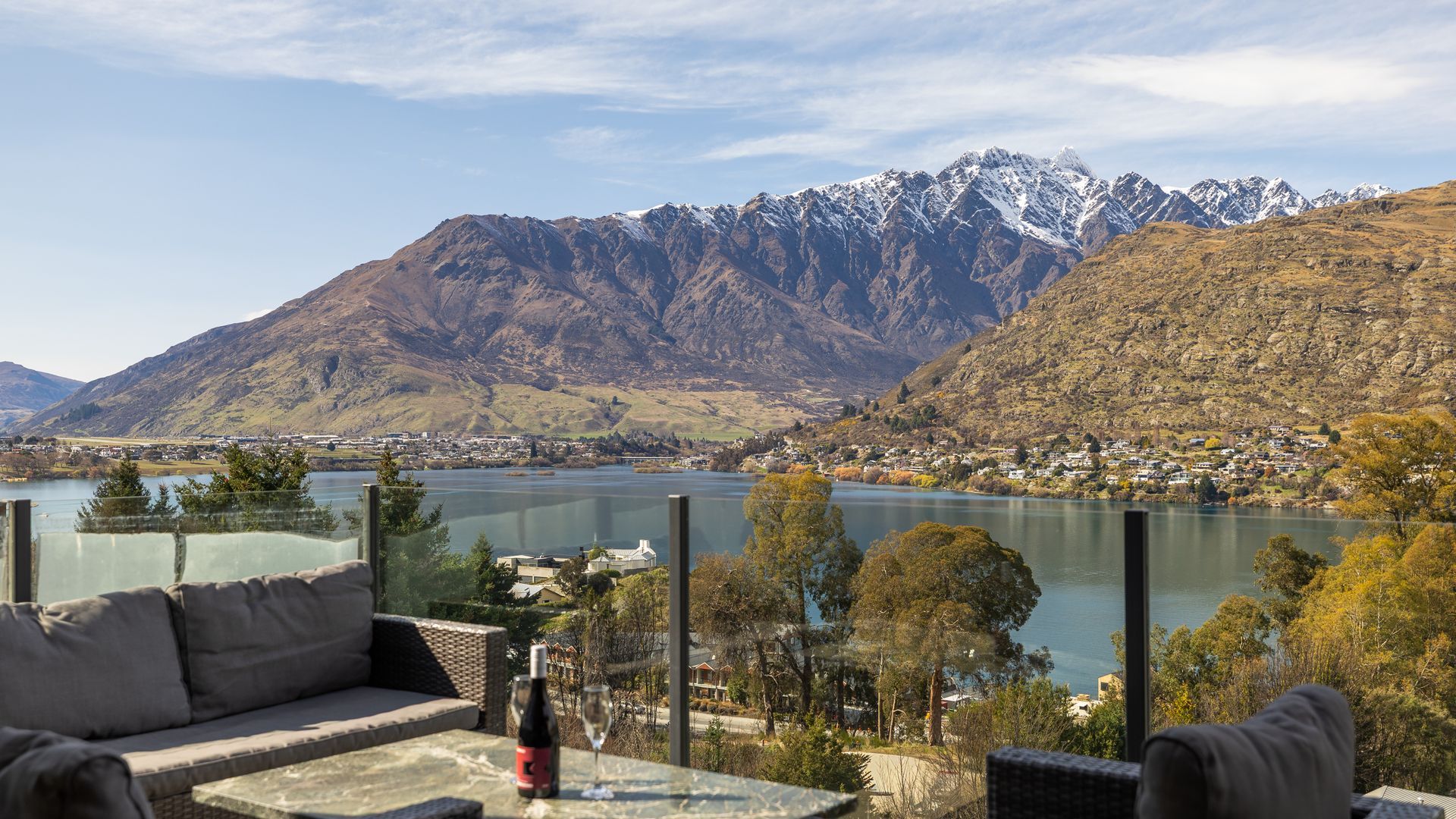 Una terrazza con vista su un lago e montagne, arredata con un divano e un tavolo con una bottiglia.