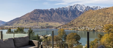 A terrace with a view of a lake and mountains, furnished with a sofa and a table with a bottle.