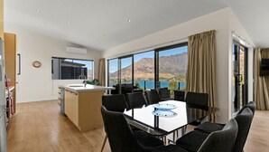 Una cocina moderna con una isla central, un comedor con mesa y sillas, y ventanas amplias con vistas panorámicas a la montaña.
