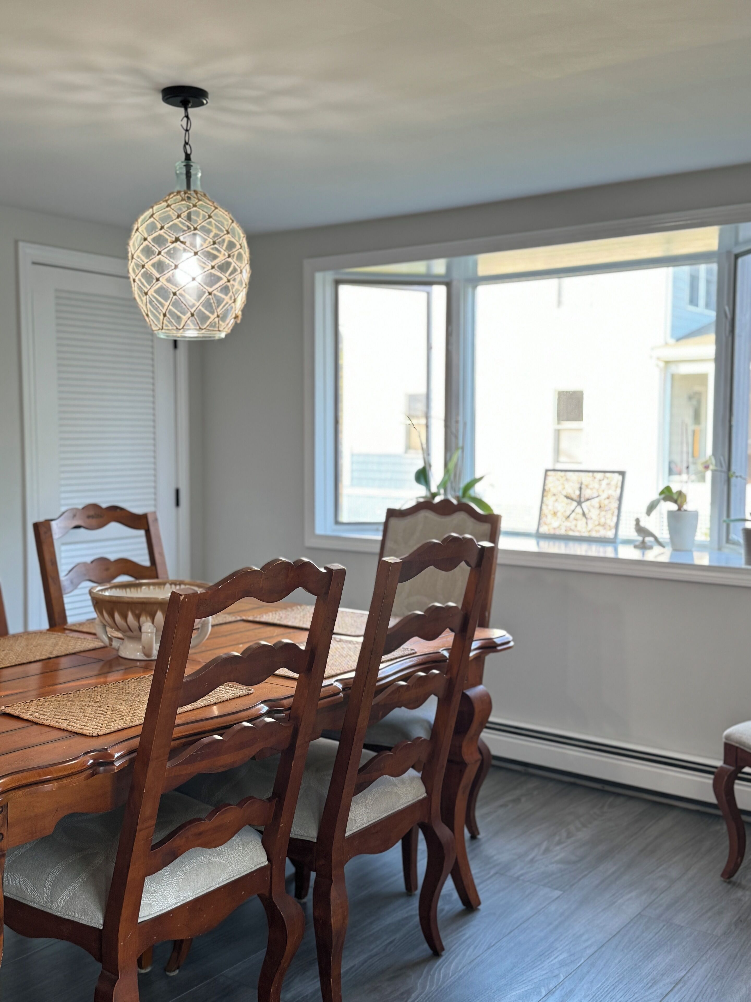 A dining area with a wooden table and chairs, a woven placemat, and a hanging light fixture.