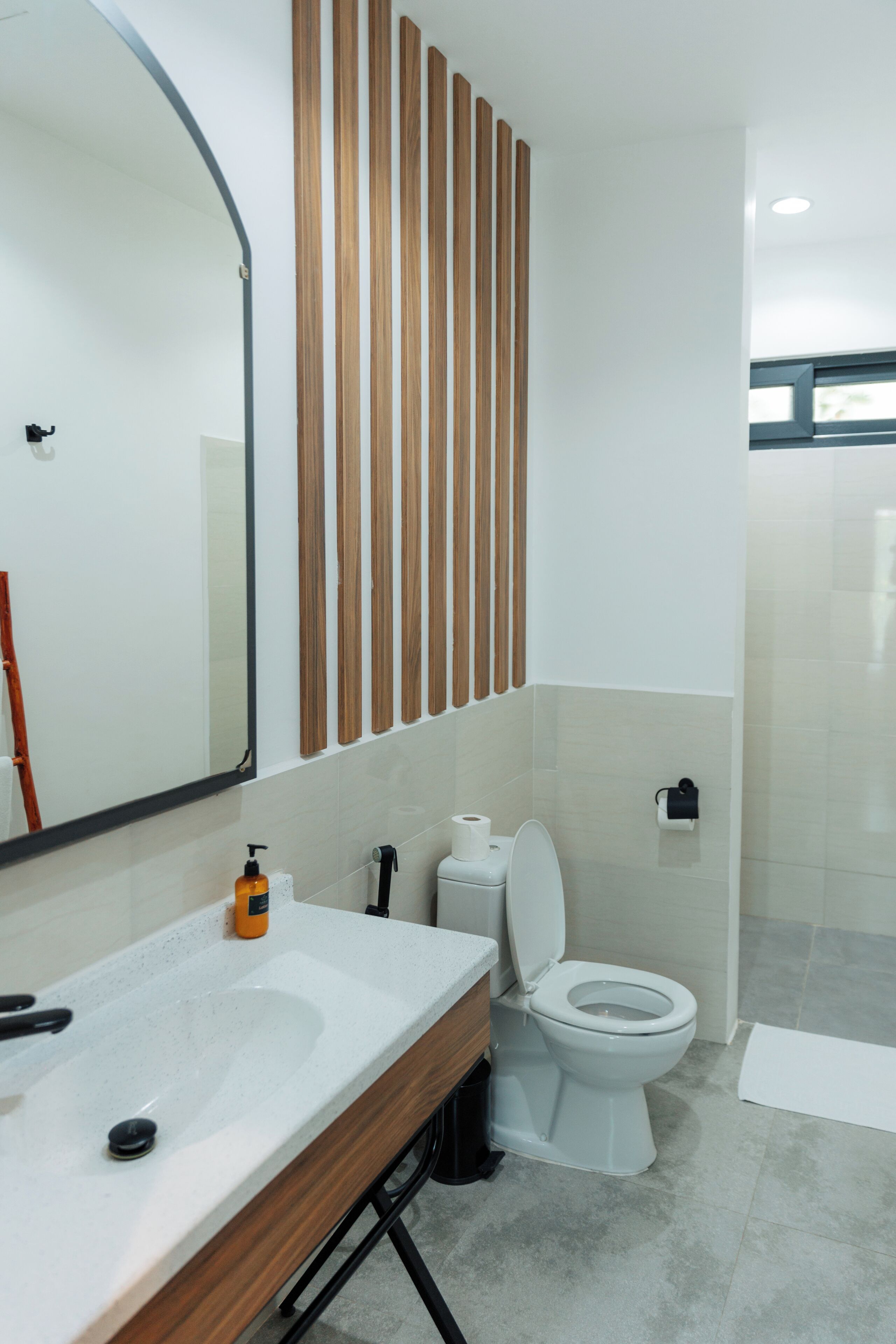 Un baño moderno con un panel de pared de madera, un espejo grande, un lavamanos blanco y un inodoro.
