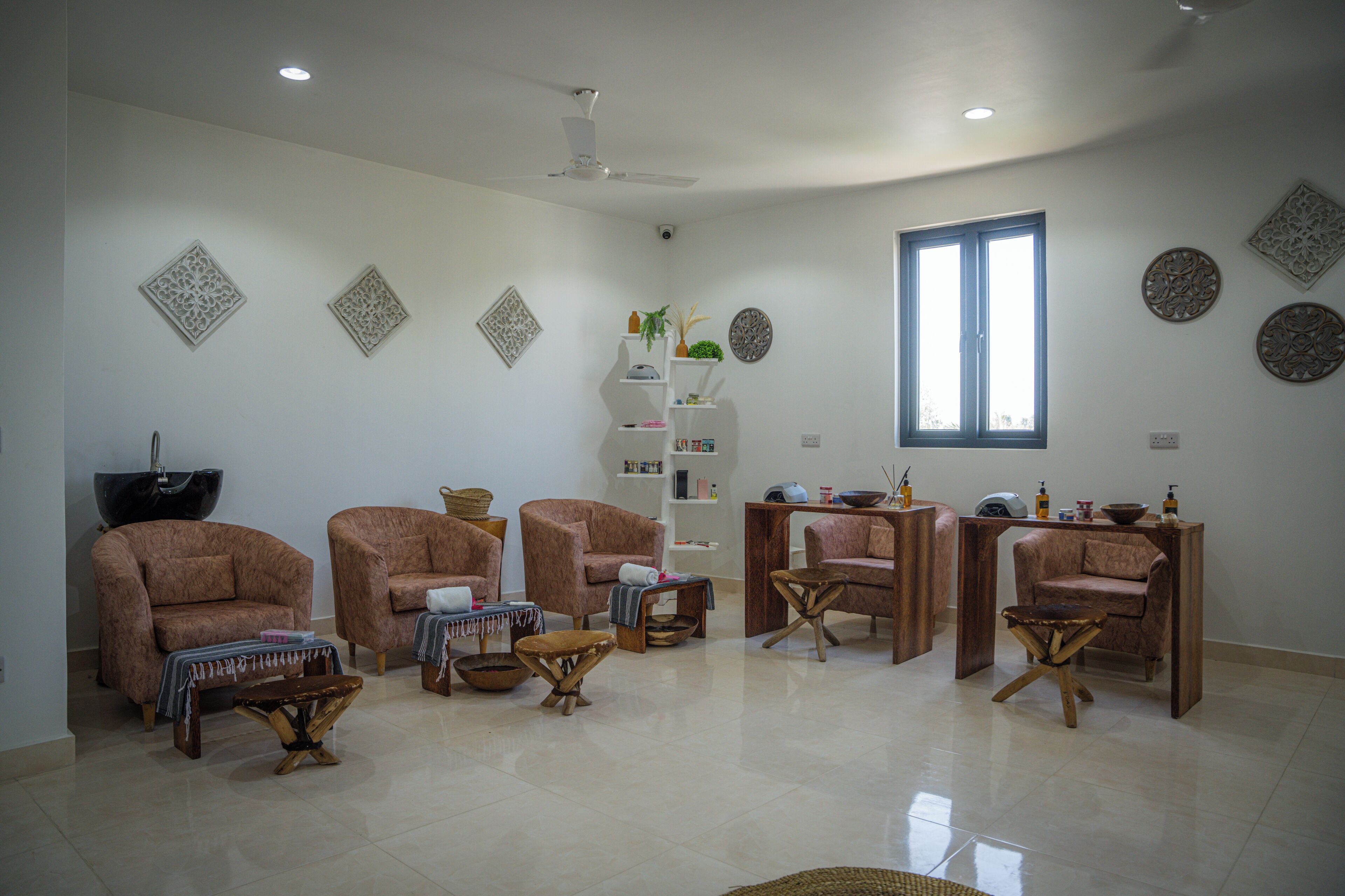 A spacious living room with a high ceiling, a ceiling fan, and a large window providing natural light. There are several armchairs and a wooden coffee table.