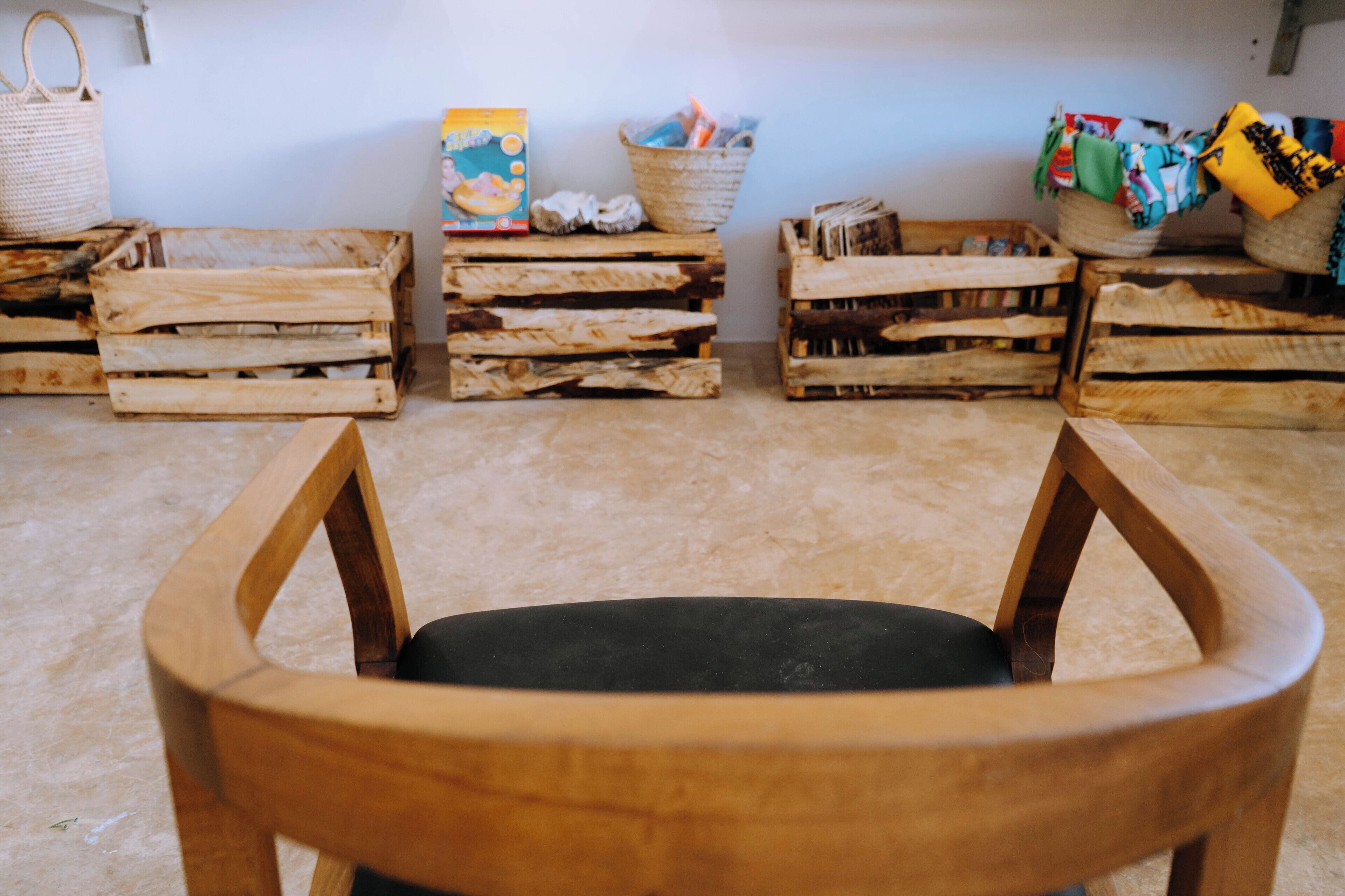Een kamer met een rij houten kisten, een geweven mand en een houten stoel op de voorgrond.