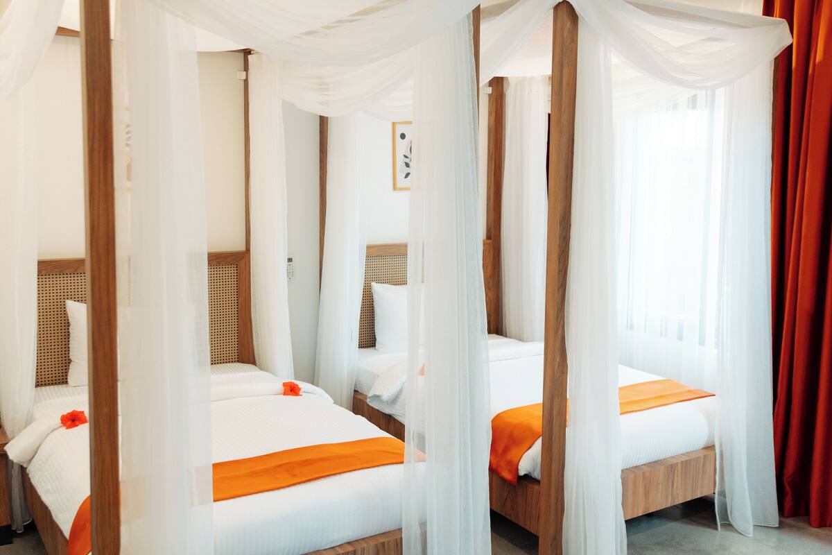 Habitació d'hotel amb tres llits, cadascun amb dosser i roba de llit taronja.