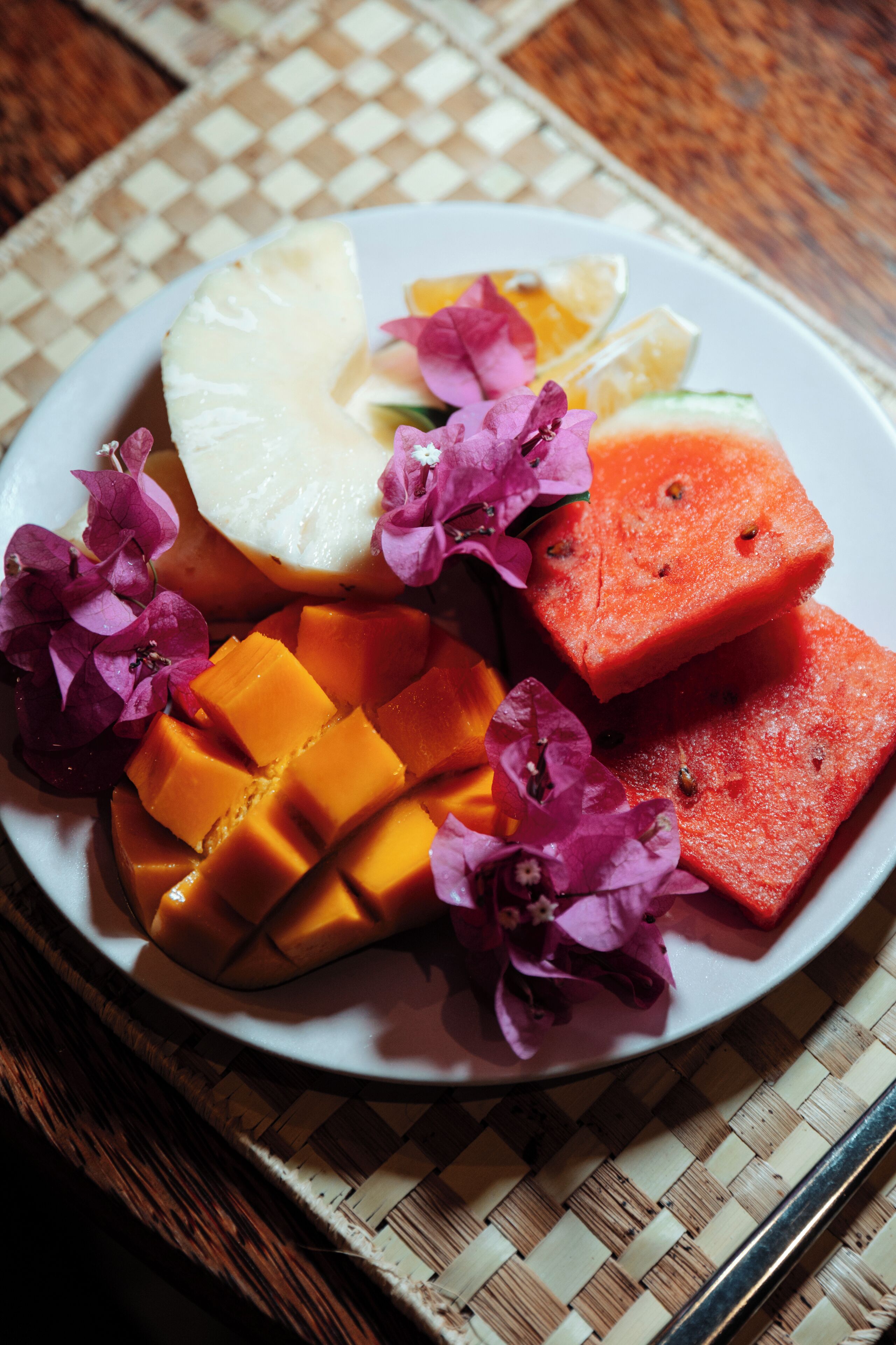 A plate with sliced mango, watermelon, and pineapple on a woven mat.