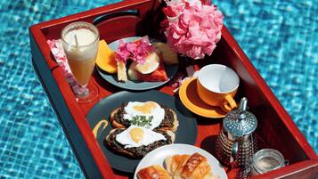 Bandeja con alimentos para el desayuno, como tostadas, huevos, fruta y una bebida, colocada al lado de una piscina.