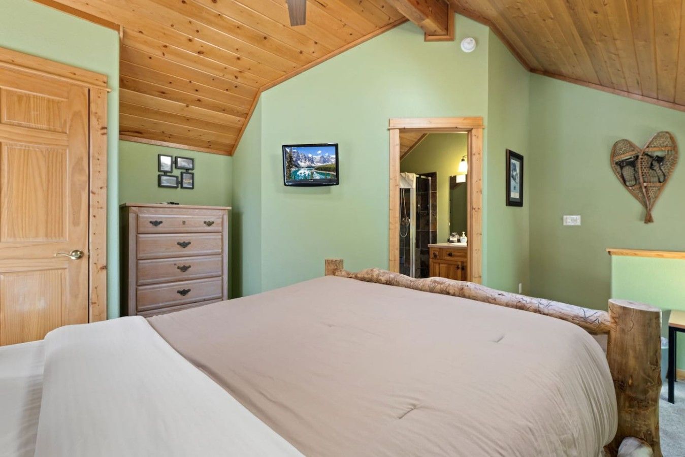 Un dormitorio con techo de madera, una cama, un aparador, un espejo y un cuadro en la pared.