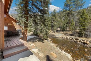 A wooden cabin with a deck, a grill, and a sign welcoming guests. - Fall River Condo • River Views • Near RMNP (Estes Park)