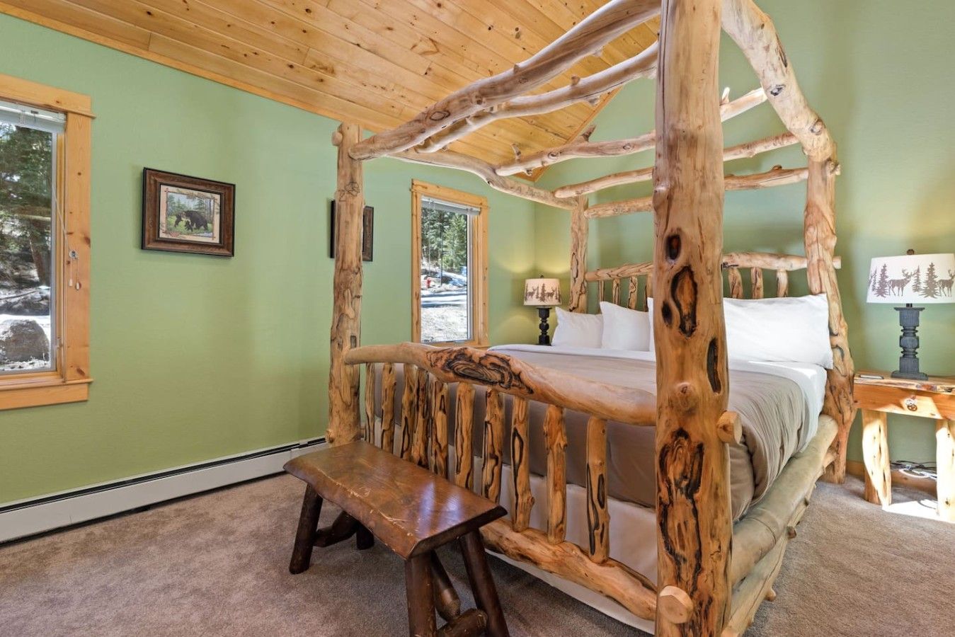 A four-poster bed with a wooden frame, a bench at the foot of the bed, and a window with a view of trees.