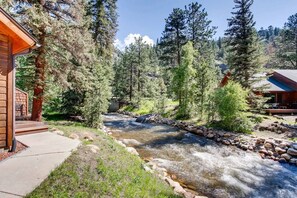 A cabin with a stone-lined stream, surrounded by dense forest. - Fall River Condo • River Views • Near RMNP (Estes Park)
