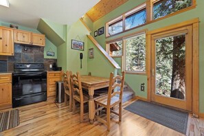 A kitchen with wooden cabinets, a stove, and a dining table with chairs. - Fall River Condo • River Views • Near RMNP (Estes Park)