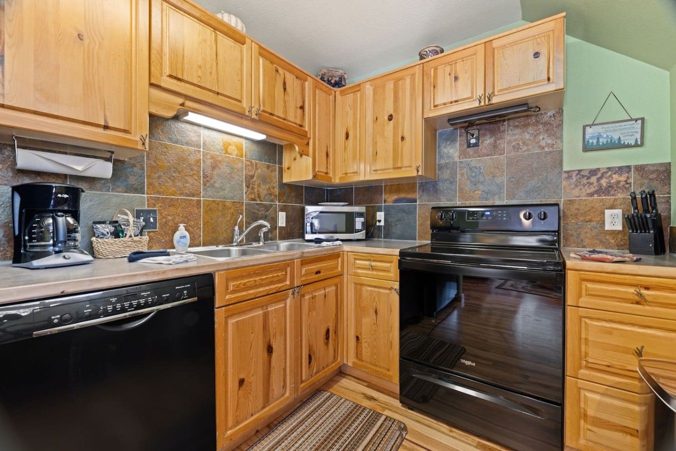 Una cocina con gabinetes de madera, lavavajillas, estufa y microondas.