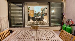A patio with a wooden table and chairs, a bench, and a sliding glass door leading to an interior dining area.