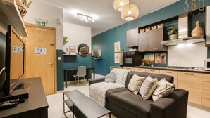 A modern living room with a sofa, a coffee table, and a TV. There is a kitchen area with cabinets and a stove. - 2BR + Big BBQ Terrace | Heart of St Julian`s (St. Julian`s)