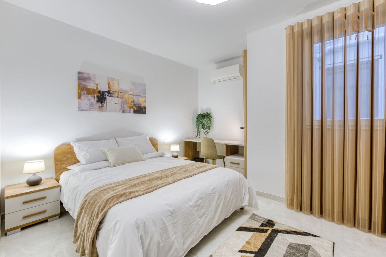Un dormitorio moderno con una cama grande, mesitas de noche, un escritorio y una ventana con cortinas.