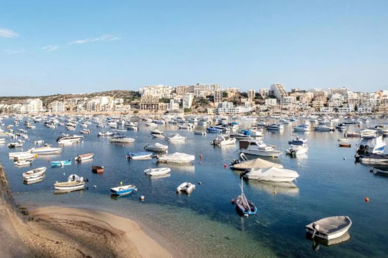 Una marina llena de barcos, una playa de arena y un paisaje urbano al fondo.