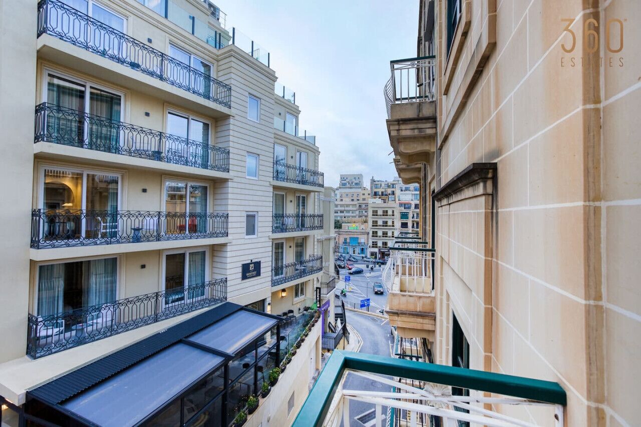 Un edificio residencial de varios pisos con balcones, vista a la calle y cielo despejado.