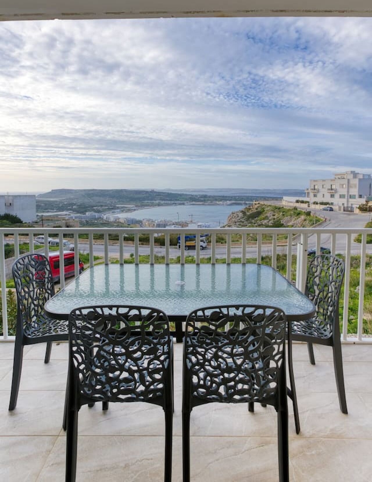 Un tavolo con piano in vetro e quattro sedie su un balcone con vista sulla costa.