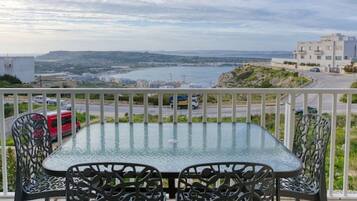 Un tavolo con piano in vetro e quattro sedie su un balcone con vista sulla costa.