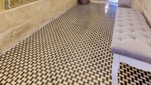 A hallway with a checkered floor, a chandelier, and a bench.