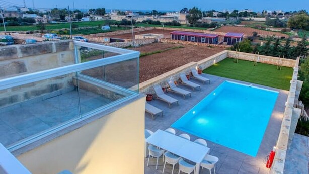 A rooftop pool with a clear view of the sea, surrounded by lounge chairs and a dining area.