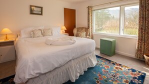 Une chambre à coucher bien aménagée, avec un grand lit, deux lampes de chevet, une chaise, une fenêtre avec des rideaux et un petit pouf vert.