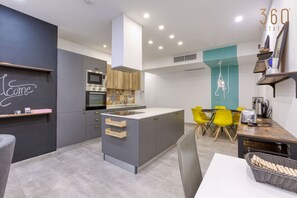 A modern kitchen with grey cabinets, a central island, and a dining area with yellow chairs.
