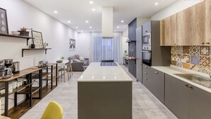A modern kitchen with a central island, built-in appliances, and a dining area with a yellow chair. - Designer 3BR home with Private Balcony in Gzira (Il-Gżira)