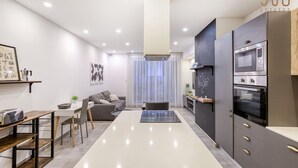 A modern kitchen with a built-in oven and microwave, a dining area with a table and chairs, and a living space with a sofa and a coffee table. - Designer 3BR home with Private Balcony in Gzira (Il-Gżira)