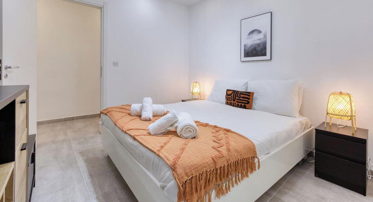 Ein modernes Schlafzimmer mit Bett, Nachttischlampen, einem Nachttisch und einer Tür.