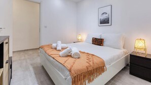 A modern bedroom with a bed, bedside lamps, a nightstand, and a door. - Designer 3BR home with Private Balcony in Gzira (Il-Gżira)