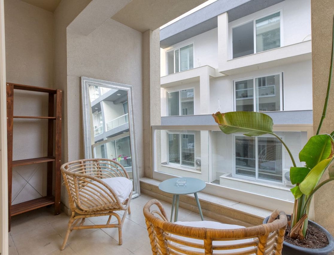 Ein Balkon mit Korbstühlen, einem kleinen Tisch und einem Topfpflanzen.