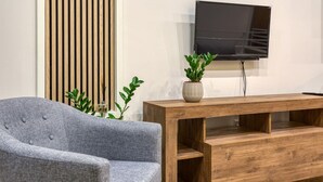 Un salon moderne avec un fauteuil gris, une console en bois et un téléviseur à écran plat fixé au mur.