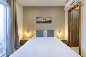 Quarto de hotel com uma cama grande, duas luminárias de cabeceira, um quadro na parede e uma porta de madeira.