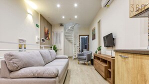 Un salon moderne comprenant un canapé, un fauteuil, un meuble en bois, un téléviseur et un escalier en colimaçon.