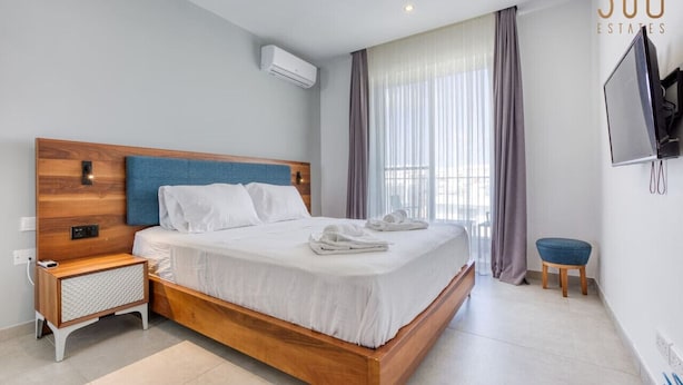 A modern hotel room with a wooden bed, a nightstand, a TV, and a window with curtains.