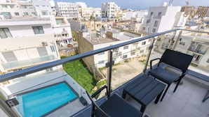 A balcony with a pool, two chairs, and a view of a residential area.