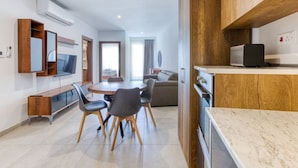 A modern hotel room with a dining area, a TV mounted on the wall, and a kitchenette.
