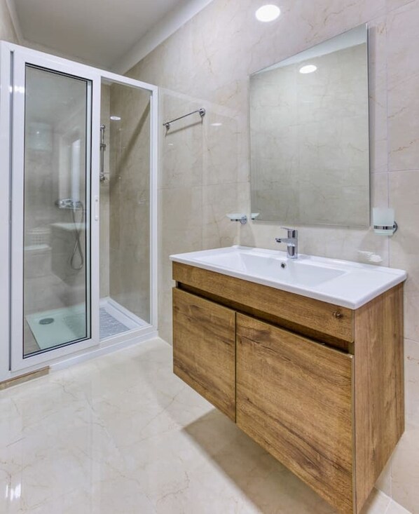 A modern bathroom with a glass shower enclosure, a wooden vanity with a mirror, and a tiled floor.