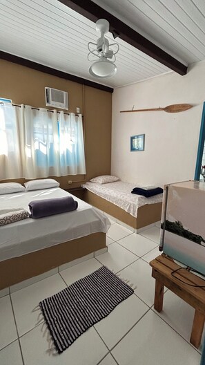 A room with two beds, a ceiling fan, a window with curtains, a picture on the wall, and a small table with a plant. - Canto do Mar  (Angra dos Reis)