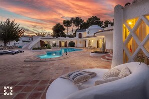 A pool area with a white infinity pool, lounge chairs, and a staircase leading to a building with arched windows. - Villa MINARET by Abahana Villas (Benissa)