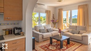 Een moderne woonkamer met een zithoek, een salontafel en een keukenhoek met kastjes en een koffieapparaat.