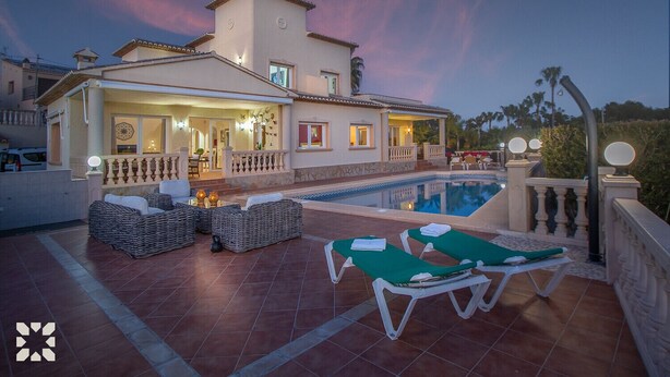 Een villa met zwembad, buitenzitplaatsen en een goed verlichte entree.