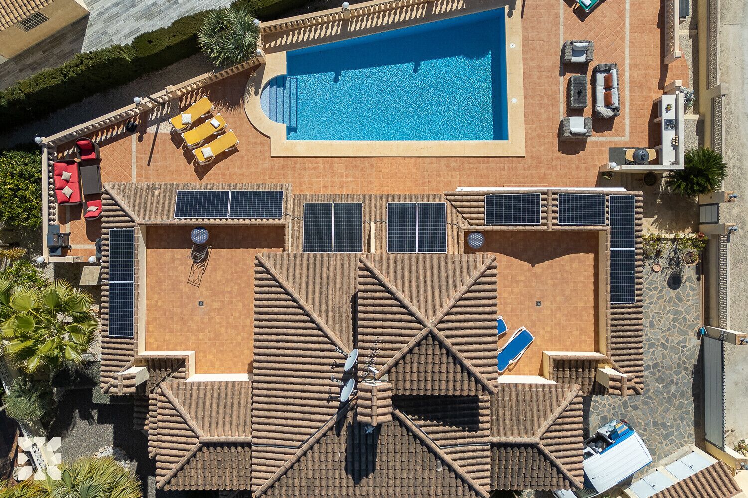An aerial view of a hotel with a swimming pool, sun loungers, and solar panels.