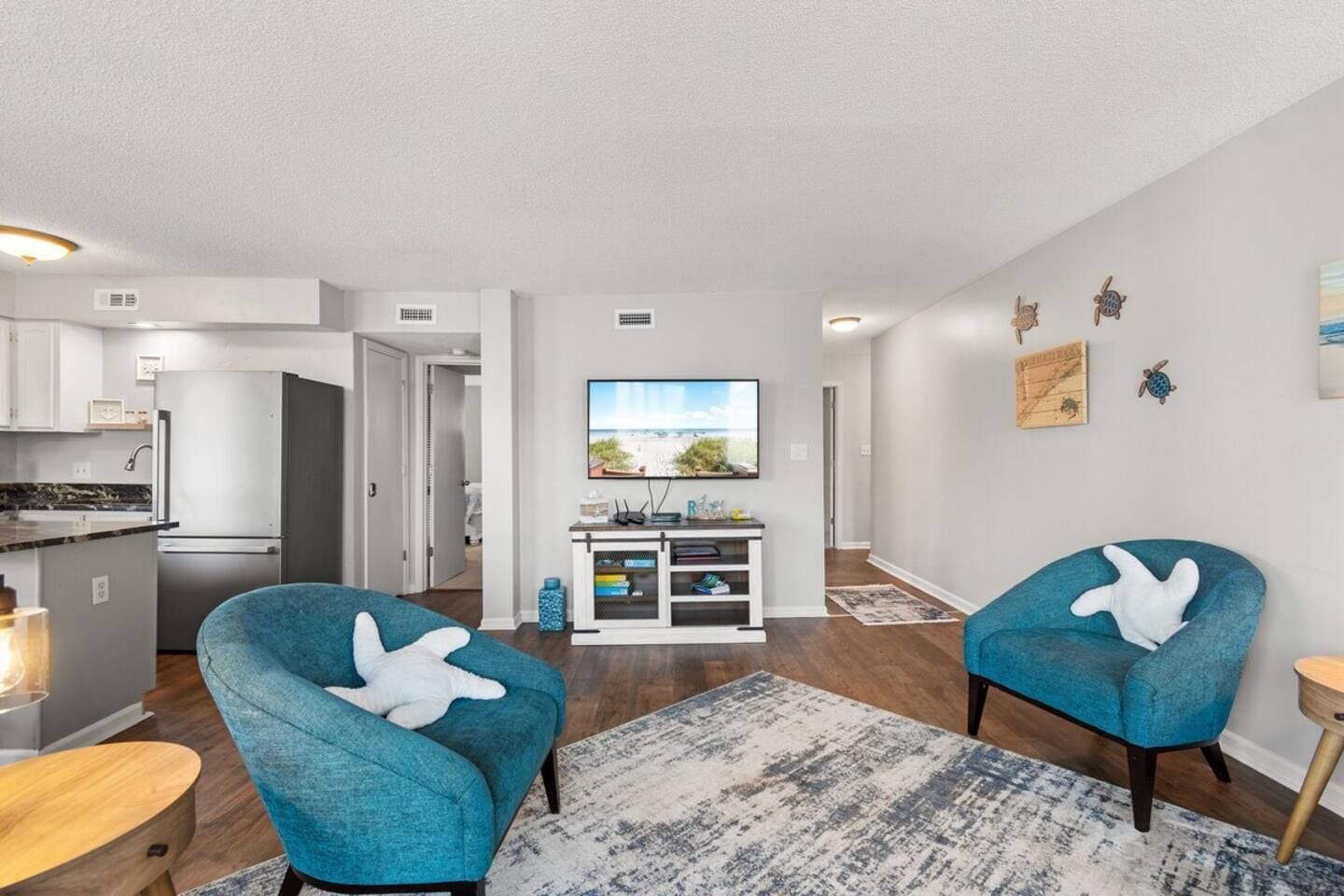 A modern living room with two blue armchairs, a coffee table, and a TV on a stand.