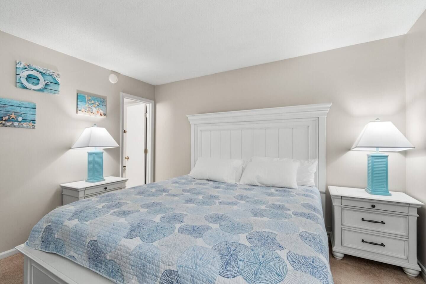 A bedroom with a large bed, two bedside tables with lamps, a door, and wall decorations.