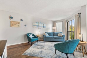 A living room with a sofa, armchairs, a coffee table, and artwork on the walls.