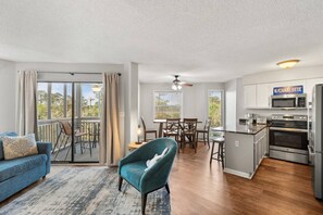 A modern living room with a sofa, a teal armchair, and a dining area with a table and chairs. - Golf Views - Outdoor pool, 3 Beds, 1 mile 2 Beach (North Myrtle Beach)