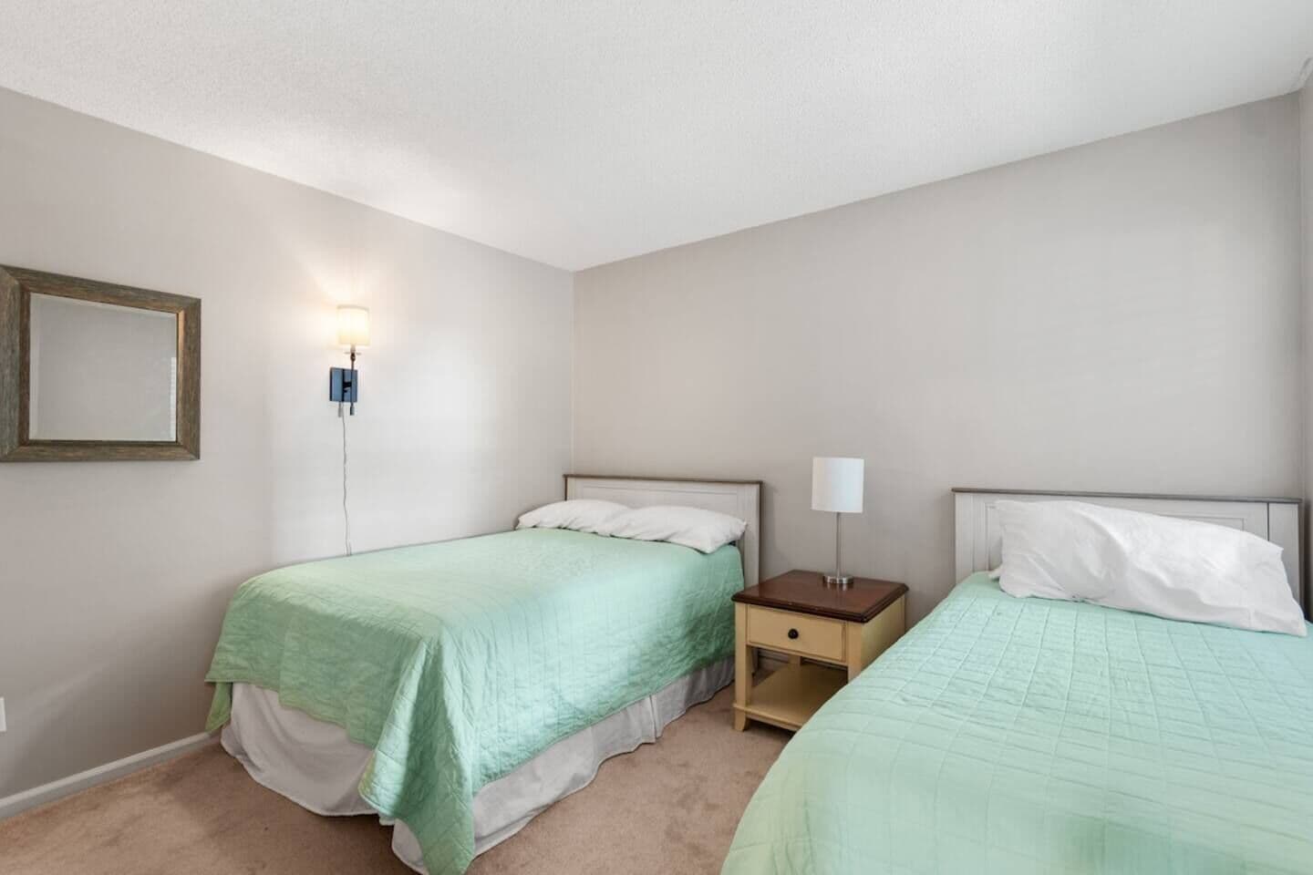 Una habitación con dos camas, una mesita de noche con lámpara y una lámpara de pared.