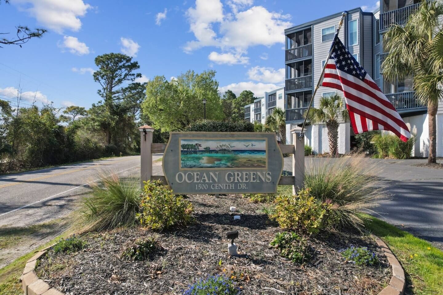 A sign for Ocean Greens at 1500 Center Dr. with an American flag.
